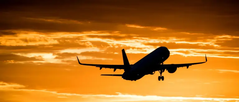 • Silhouette of a commercial aircraft in flight against a vibrant orange sunset sky.